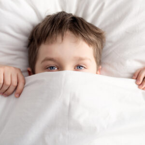 little boy in bed covering his face with white blanket